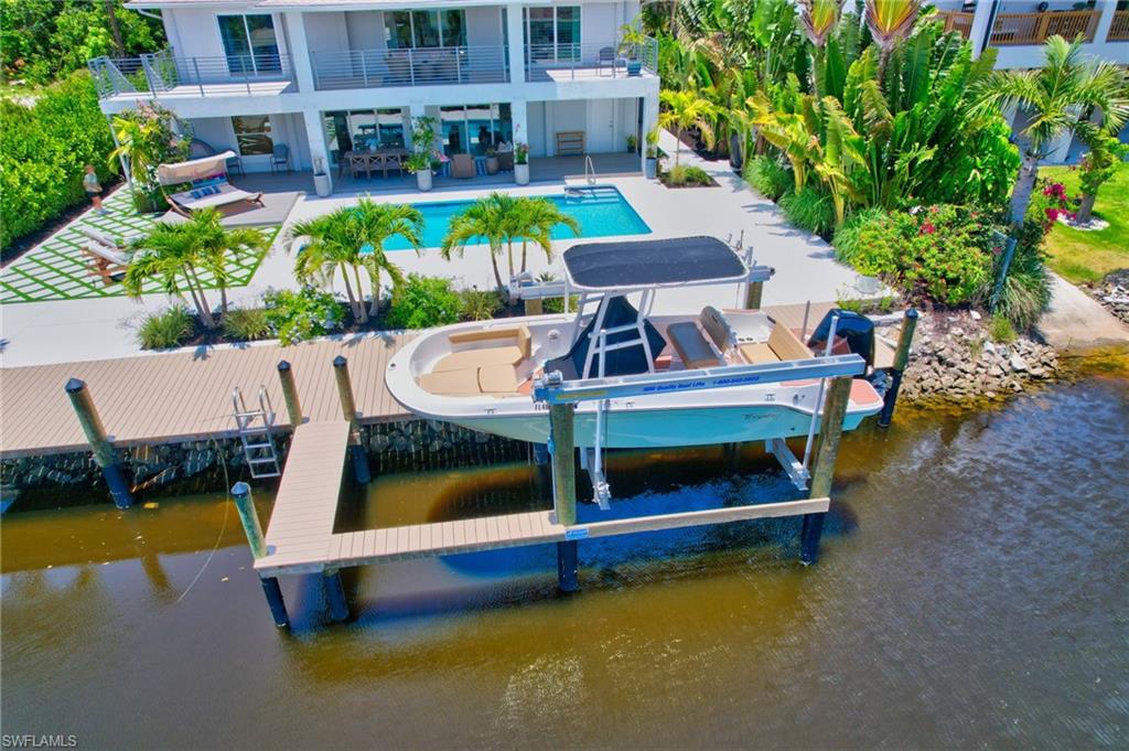 Dock area with an outdoor pool, a water view, a patio, boat lift, and outdoor seating