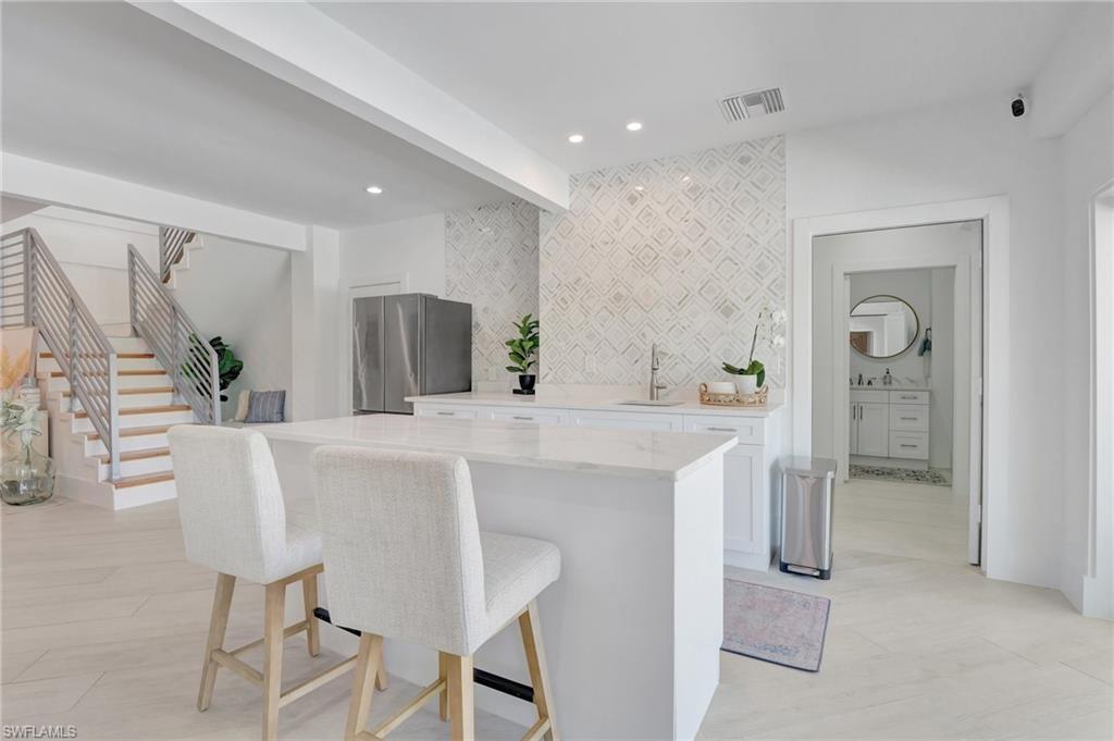Kitchen with white cabinets, freestanding refrigerator, a breakfast bar area, beam ceiling, and light stone counters