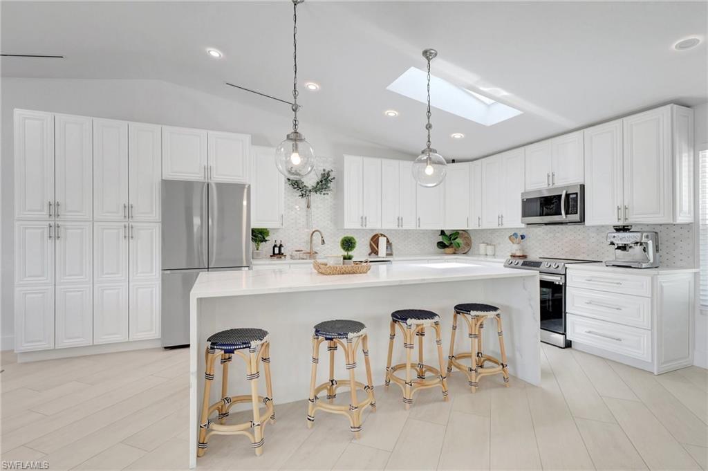 Kitchen featuring a skylight, stainless steel appliances, white cabinetry, hanging light fixtures, and lofted ceiling
