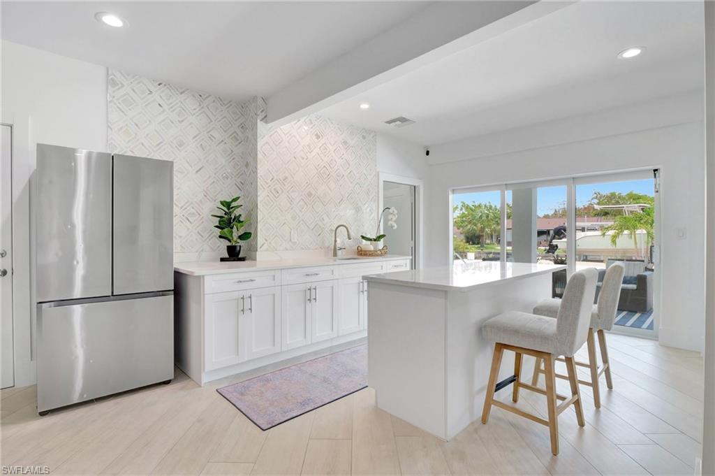Kitchen with freestanding refrigerator, white cabinets, a breakfast bar, a kitchen island, and light stone counters