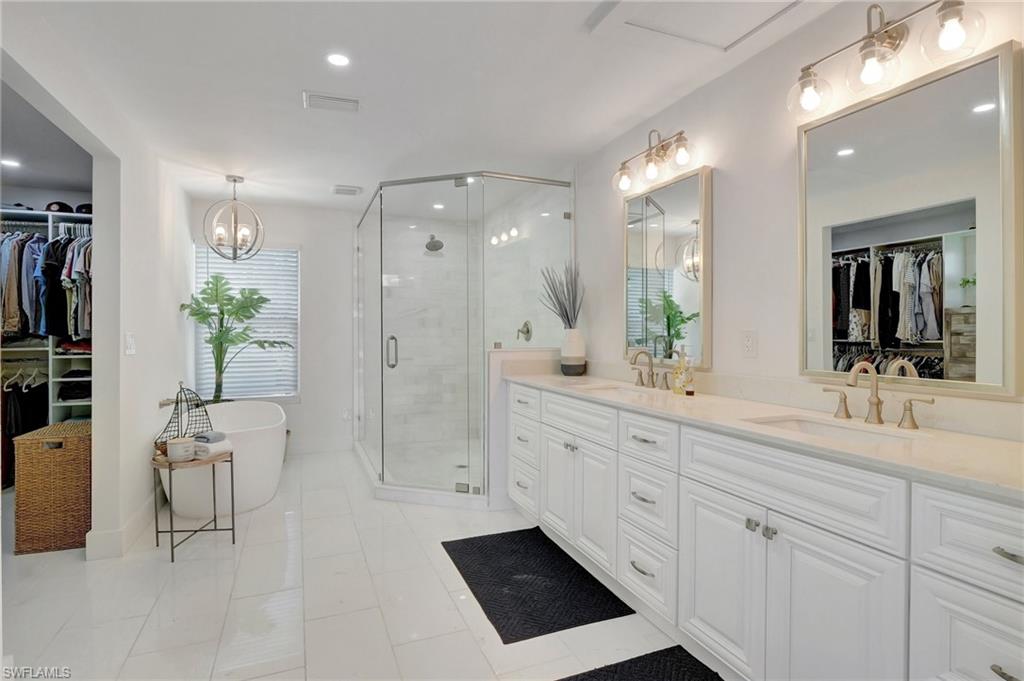 Bathroom featuring a walk in closet, double vanity, a shower stall, a freestanding bath, and a chandelier