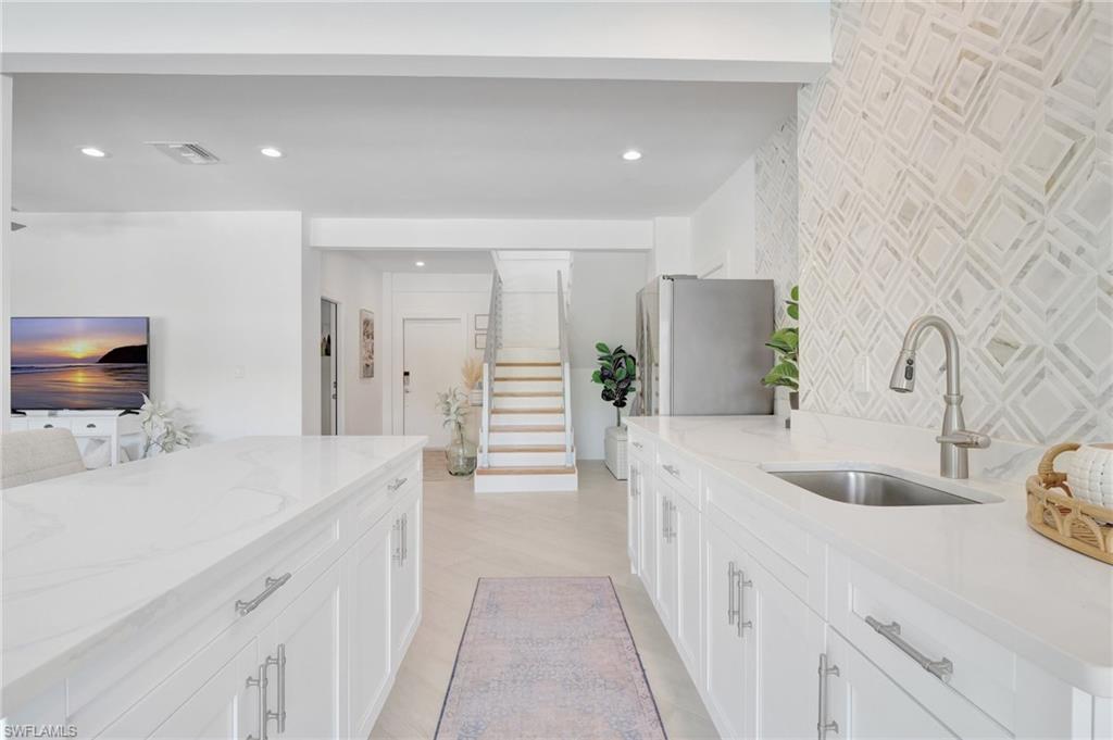 Kitchen featuring light stone counters, freestanding refrigerator, white cabinetry, and recessed lighting