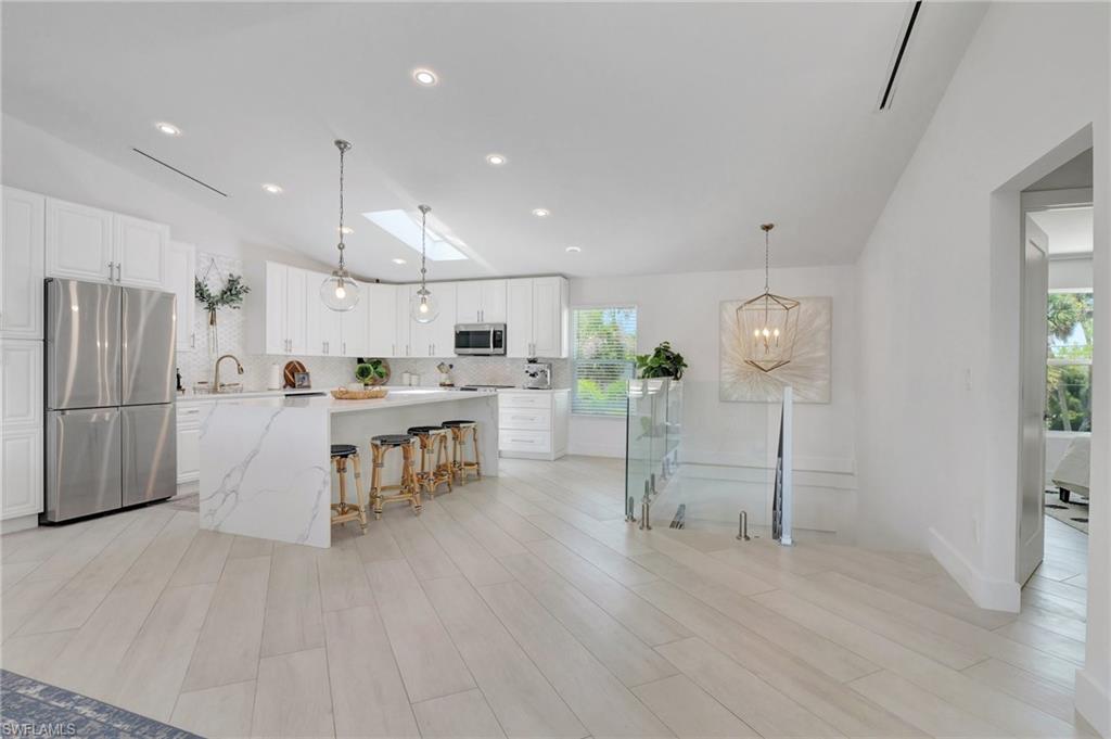 Kitchen featuring lofted ceiling, white cabinets, stainless steel appliances, a kitchen island, and decorative backsplash