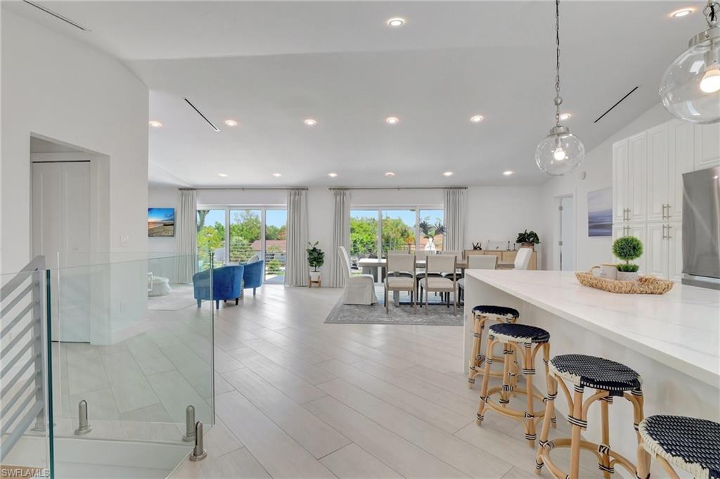 Kitchen with a breakfast bar area, white cabinetry, light wood-type flooring, light stone counters, and stainless steel refrigerator