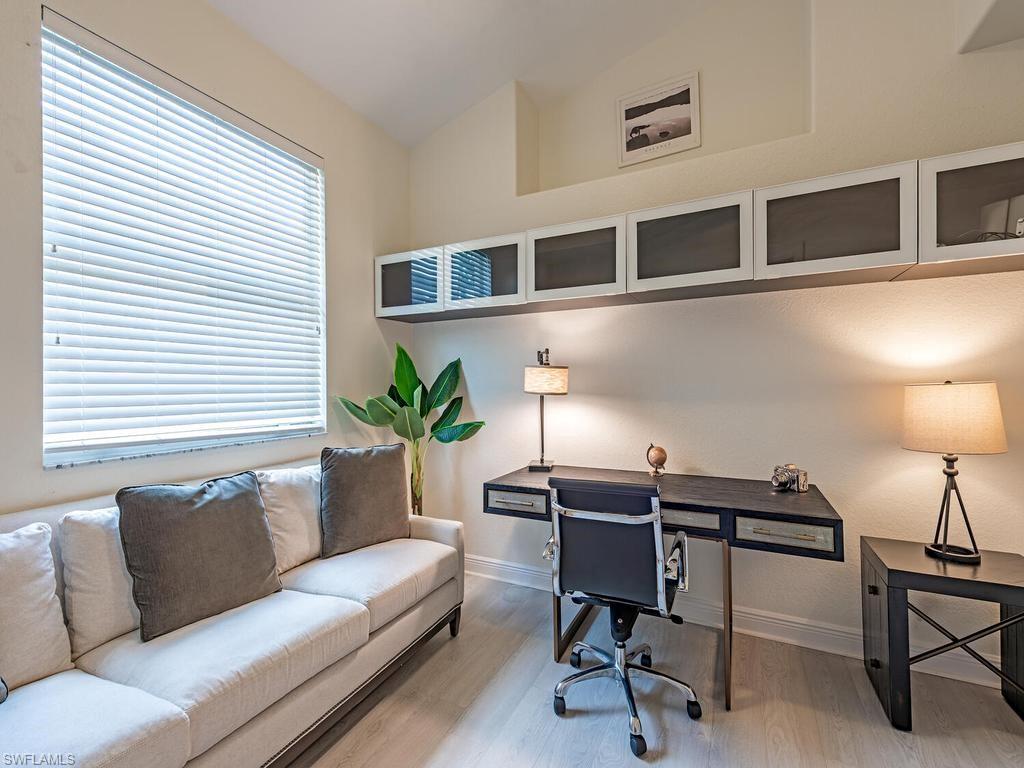 Dedicated workspace featuring wood-finish flooring, a large window with horizontal blinds, and a series of overhead frosted glass cabinets