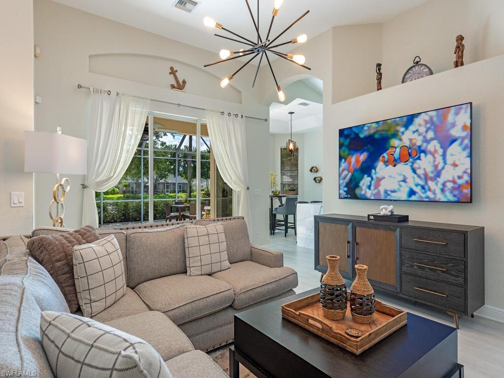 Spacious living area featuring light-toned flooring, a multi-bulb sputnik-style chandelier, and a large sliding glass door opening to an outdoor patio