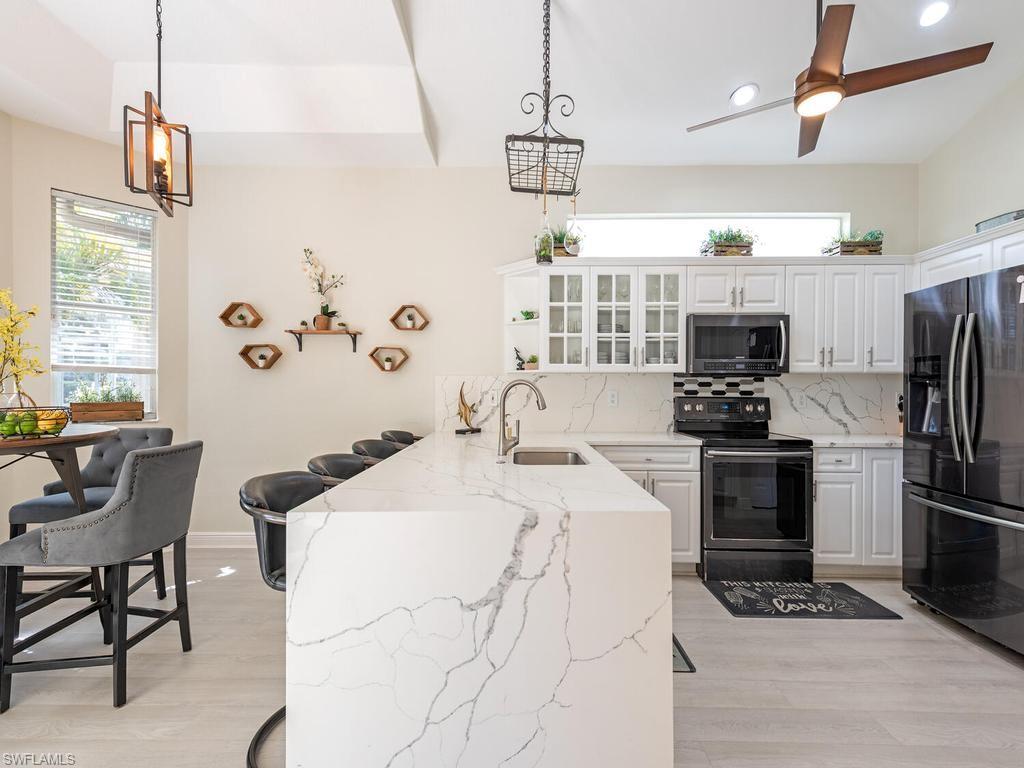 Kitchen featuring a waterfall-edge island with seating, white shaker cabinetry, stainless steel appliances, and wood-finish flooring