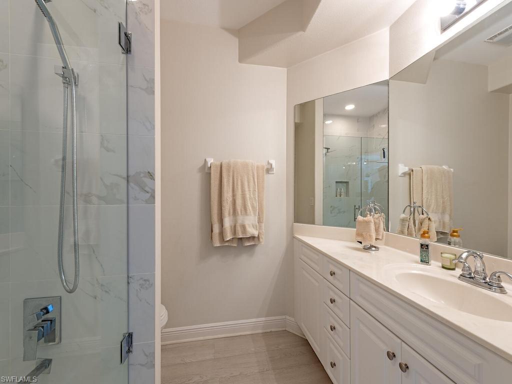 Bathroom with a spacious white vanity featuring an undermount sink, a large mirror, and a glass-enclosed shower with a handheld showerhead