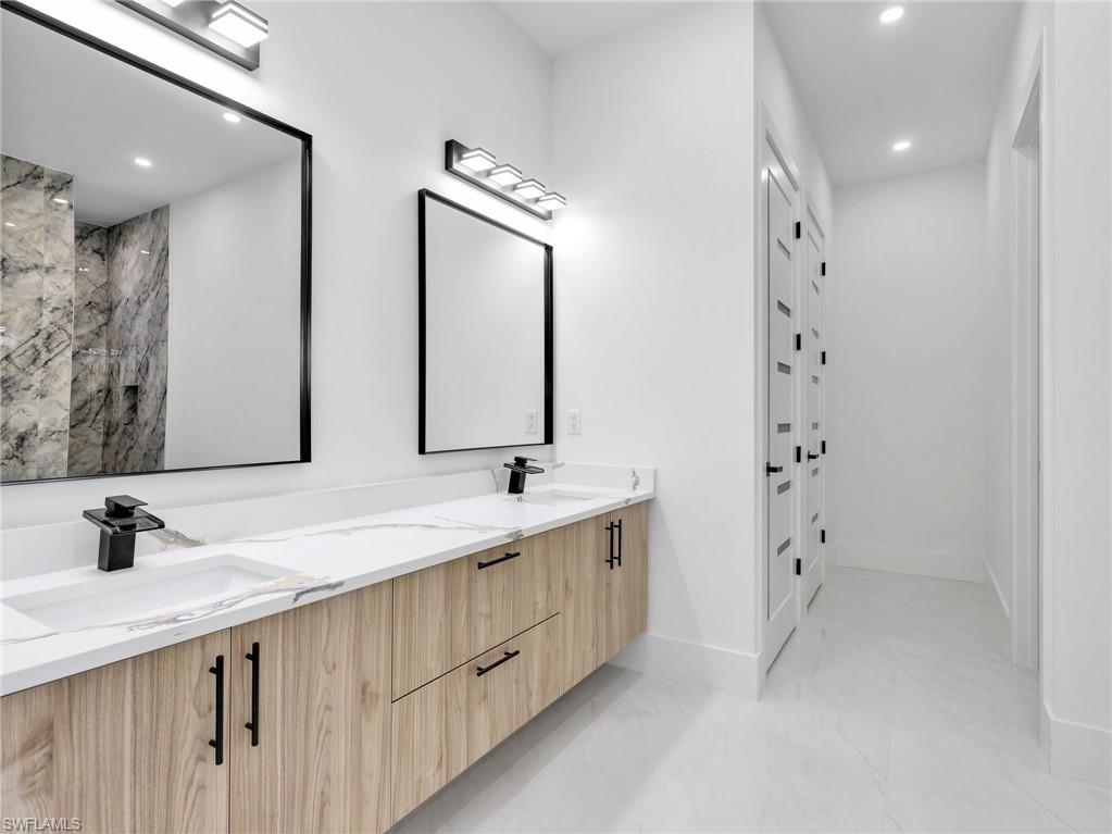 Full bath with recessed lighting, double vanity, and light marble finish floors