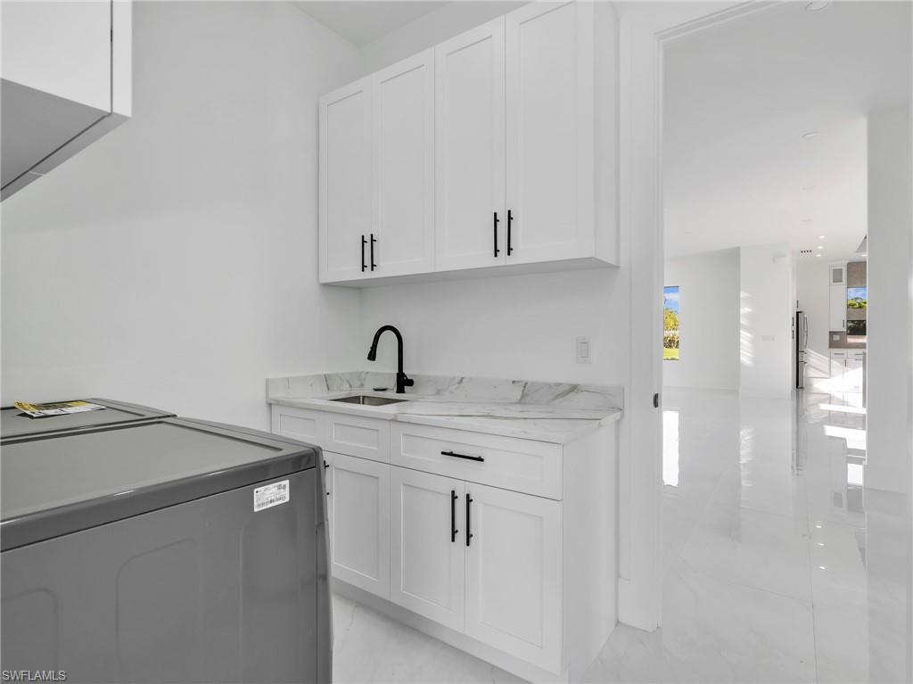 Bar featuring washer / dryer, white cabinets, and light stone counters