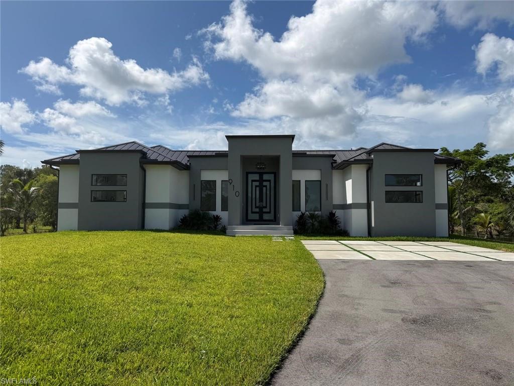 Contemporary house featuring a front yard, stucco siding, asphalt driveway, and a standing seam roof