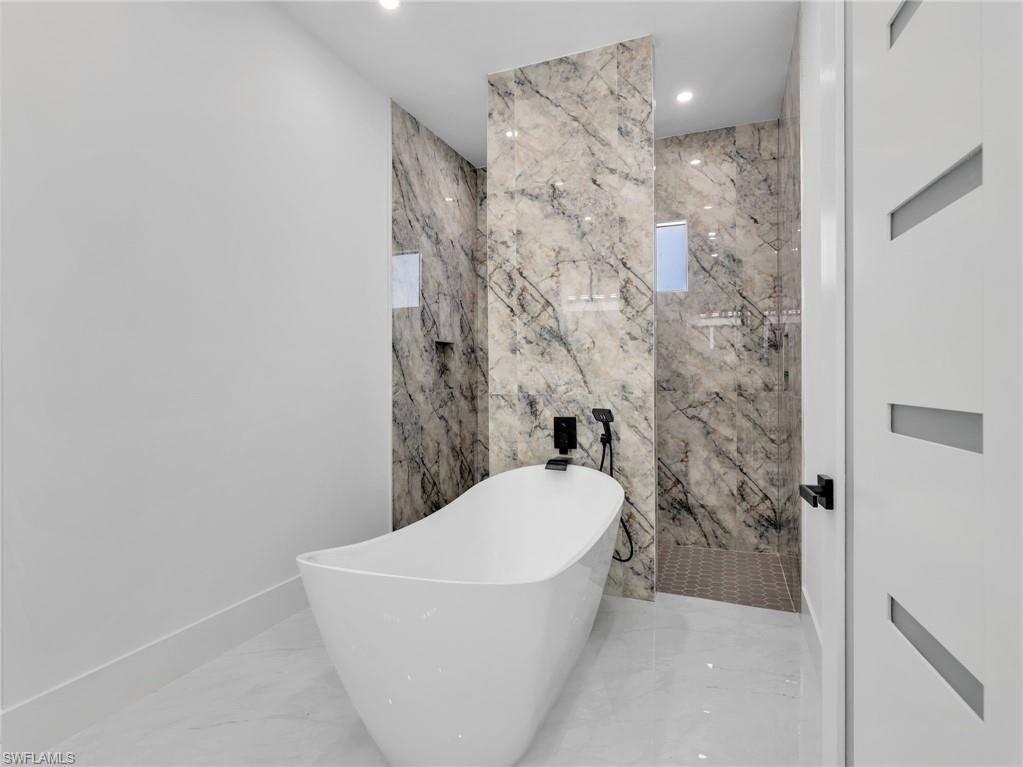 Bathroom with a freestanding tub, light marble finish flooring, stone wall, recessed lighting, and a marble finish shower