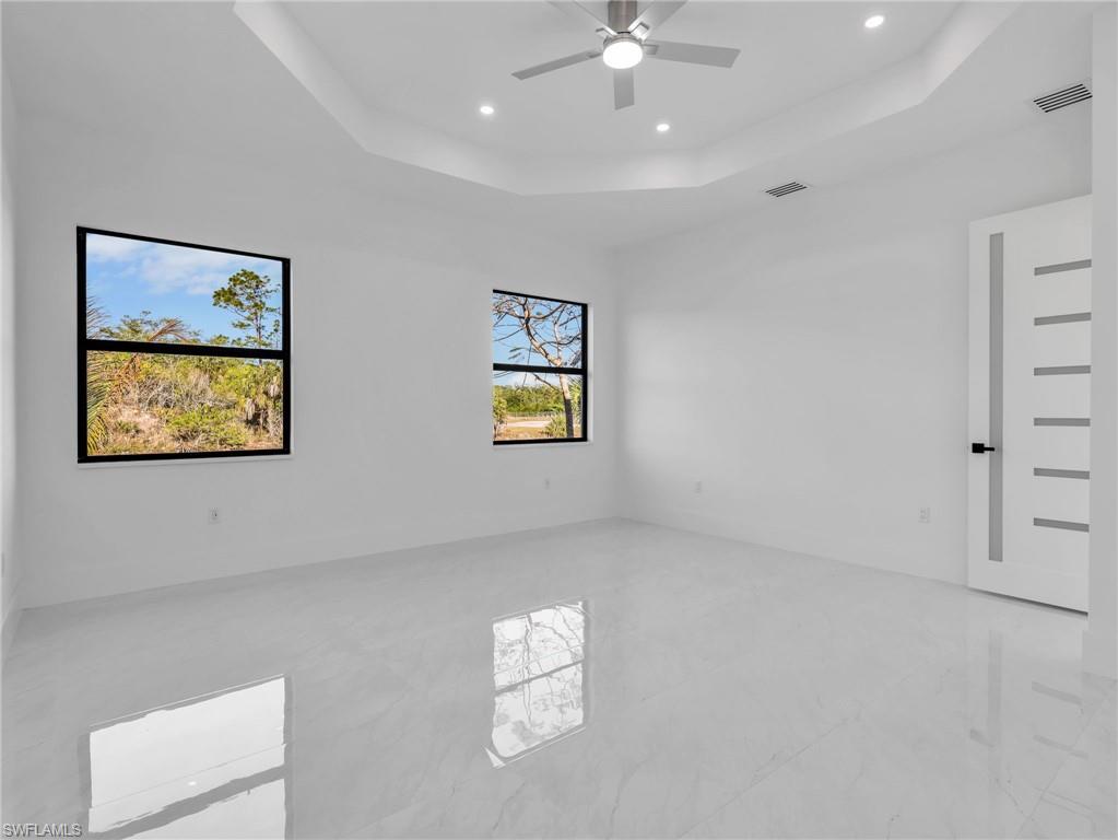 Empty room with a ceiling fan, a raised ceiling, and recessed lighting