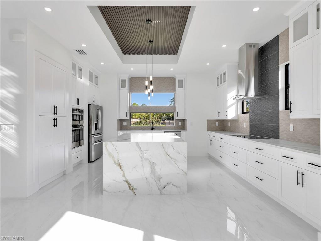 Kitchen featuring glass fronted cabinets, a kitchen island, light stone countertops, hanging lights, and stainless steel appliances