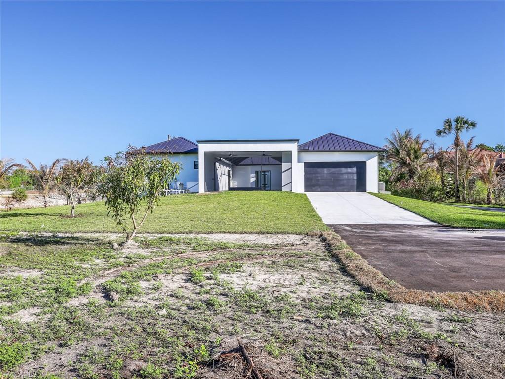Modern home with a standing seam roof, a front yard, driveway, and stucco siding