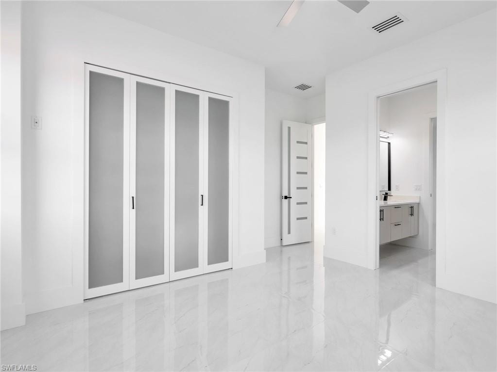 Unfurnished bedroom featuring connected bathroom, ceiling fan, light marble finish floors, and a closet