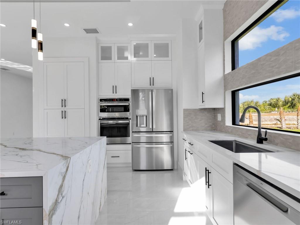 Kitchen with light stone countertops, stainless steel appliances, glass fronted cabinets, and white cabinetry
