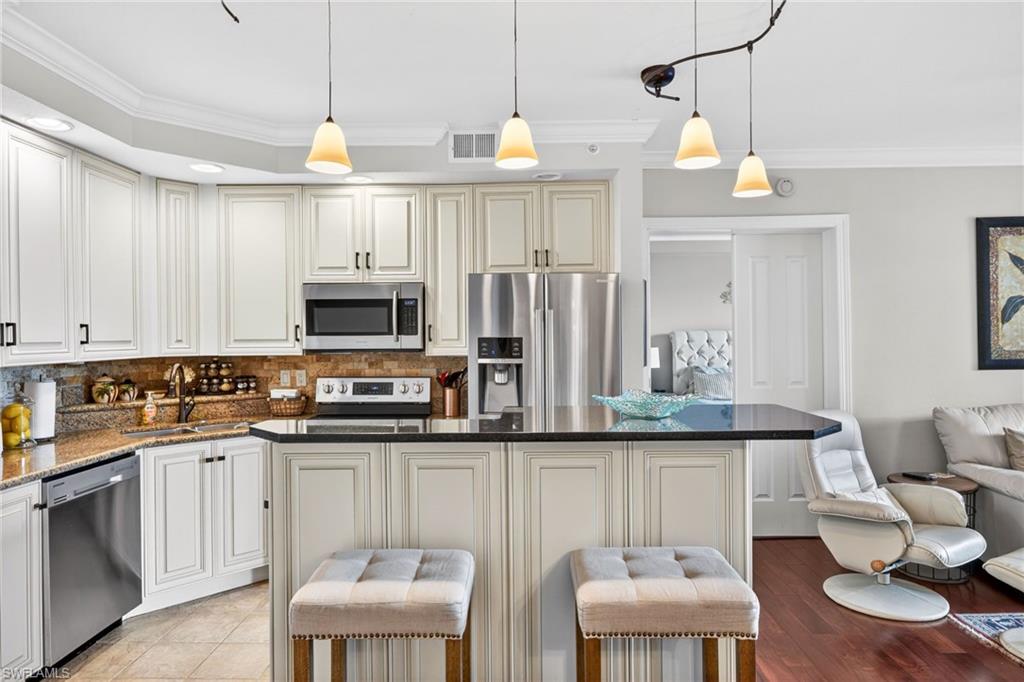 Kitchen featuring ornamental molding, decorative backsplash, a breakfast bar area, stainless steel appliances, and dark stone countertops