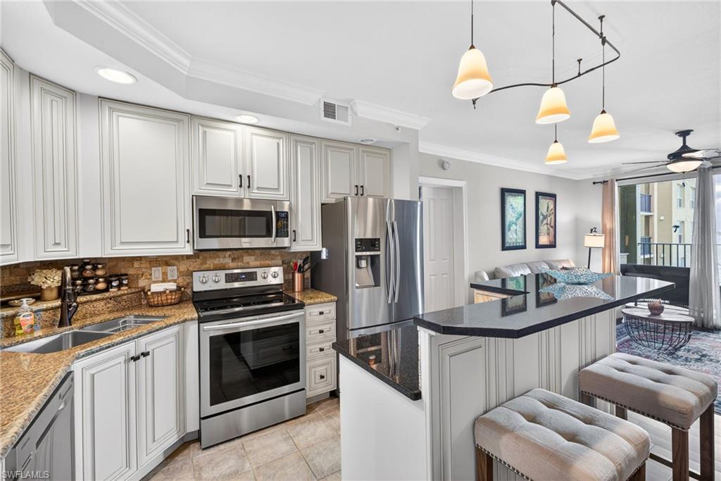 Kitchen with ornamental molding, stainless steel appliances, a kitchen island, a breakfast bar, and dark stone countertops