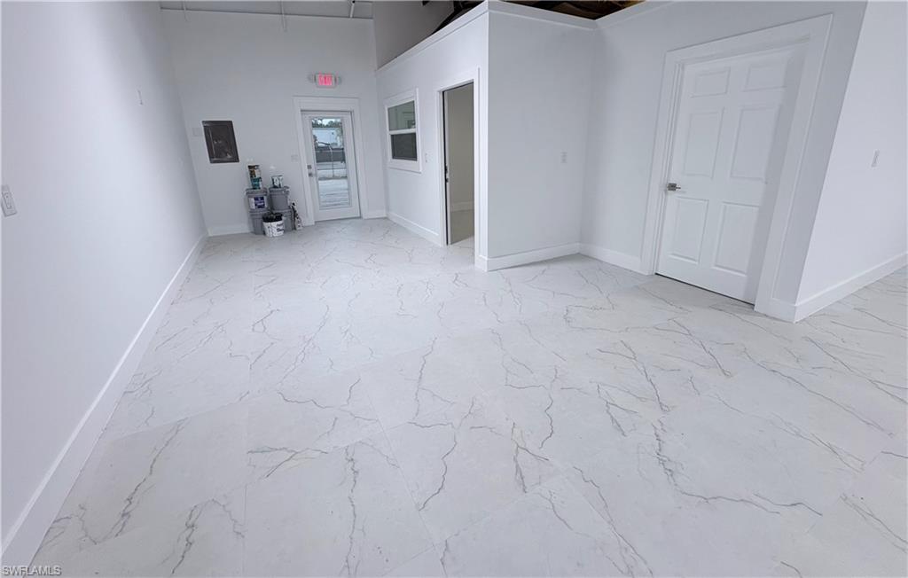 Empty room featuring light marble finish floors, electric panel, and a high ceiling