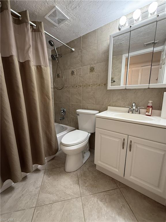 Common Bathroom featuring vanity, a textured ceiling, tile walls, and shower / bathtub combination with curtain