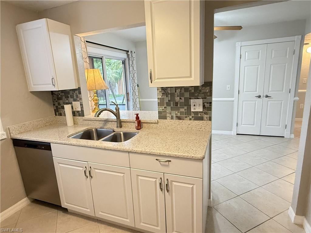 Kitchen with decorative backsplash, light stone counters, stainless steel dishwasher, light tile patterned flooring, and white cabinets