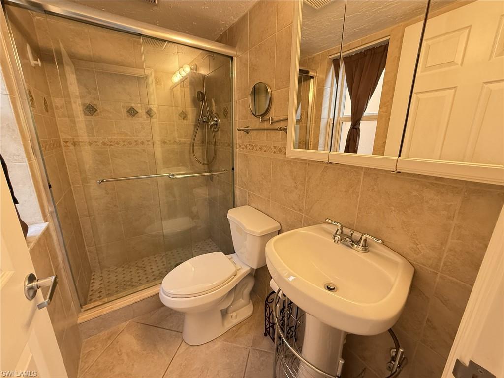 Bathroom associated with 1st bedroom featuring tile walls, a shower stall, and light tile patterned flooring