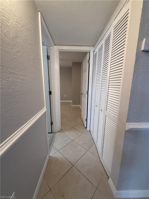 Corridor with a textured wall and light tile patterned floors that leads to common bathroom and 2nd bedroom