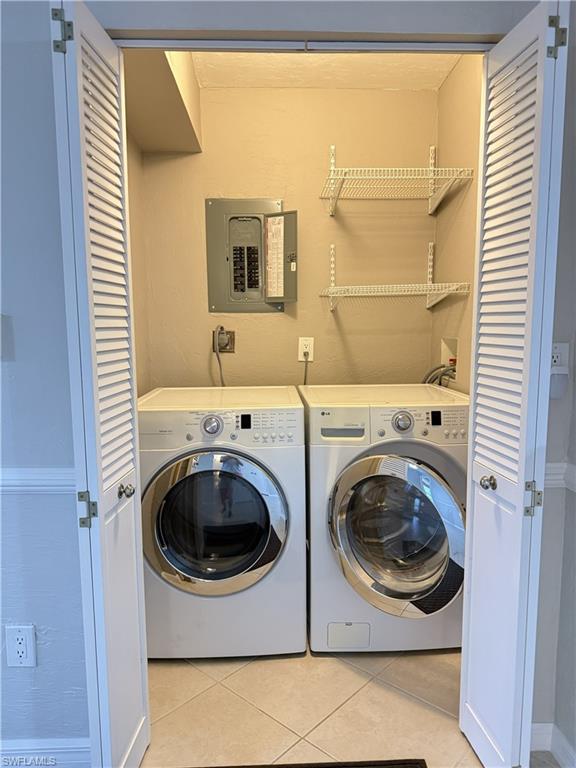 Laundry area with electric panel, light tile patterned floors, and independent washer and dryer