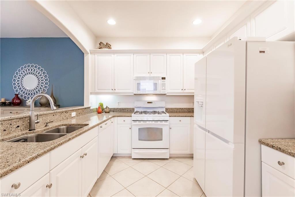 Kitchen with white appliances, white cabinets, light stone countertops, light tile patterned floors, and recessed lighting