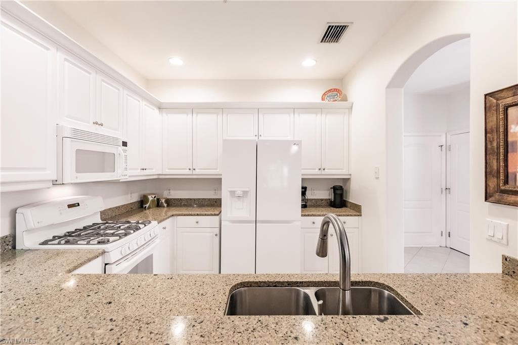 Kitchen featuring white cabinets, white appliances, light stone counters, and arched walkways