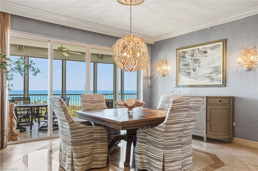 Dining area with inlaid floor details, a Gulf view, ornamental molding, and a ceiling fan