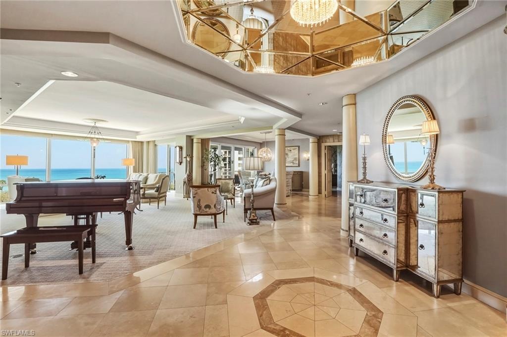 Foyer entrance with a chandelier, decorative columns, a raised ceiling, light tile patterned floors, and inlaid floor details