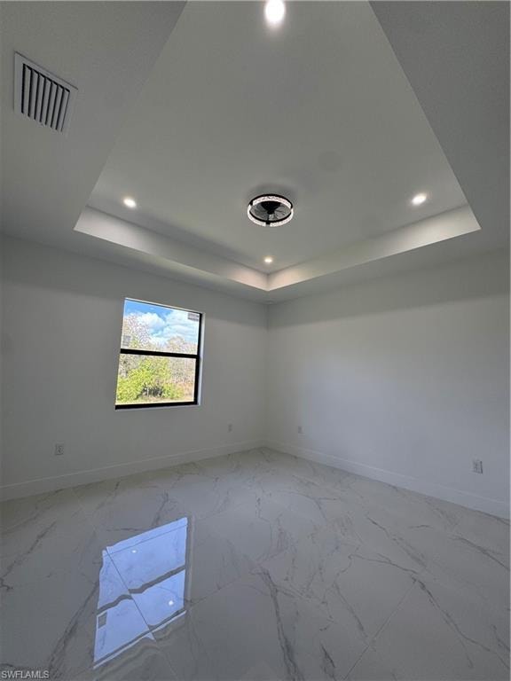 Spare room featuring recessed lighting, a tray ceiling, and light marble finish floors
