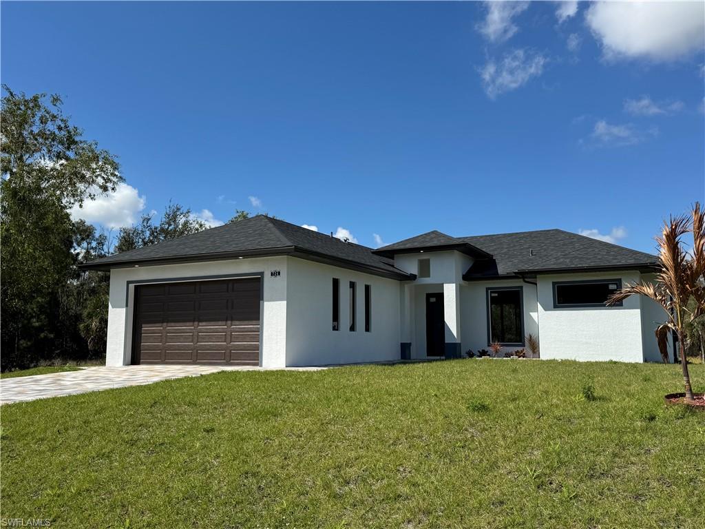 Prairie-style home featuring a front lawn, stucco siding, a garage, and driveway