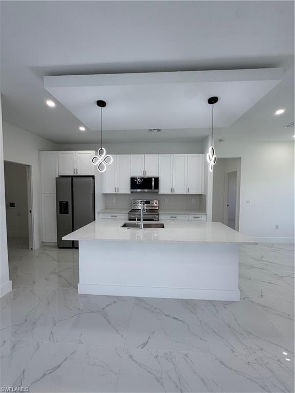 Kitchen with white cabinetry, stainless steel appliances, light stone countertops, a center island with sink, and decorative light fixtures