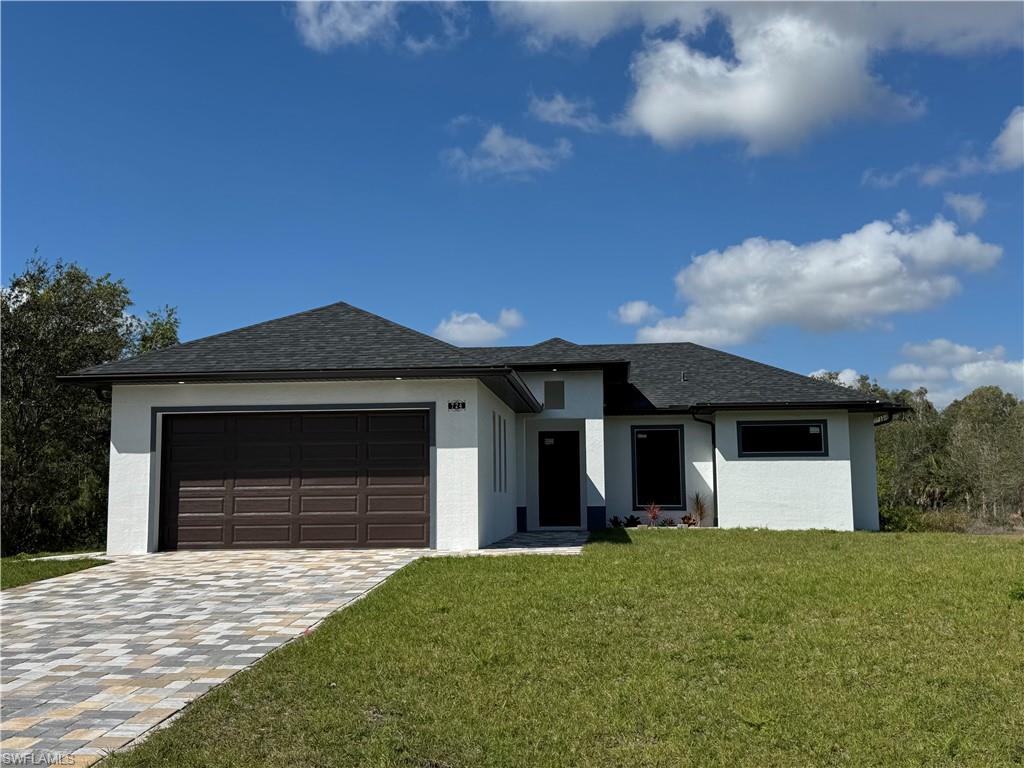 Prairie-style home with a front yard, stucco siding, an attached garage, and driveway