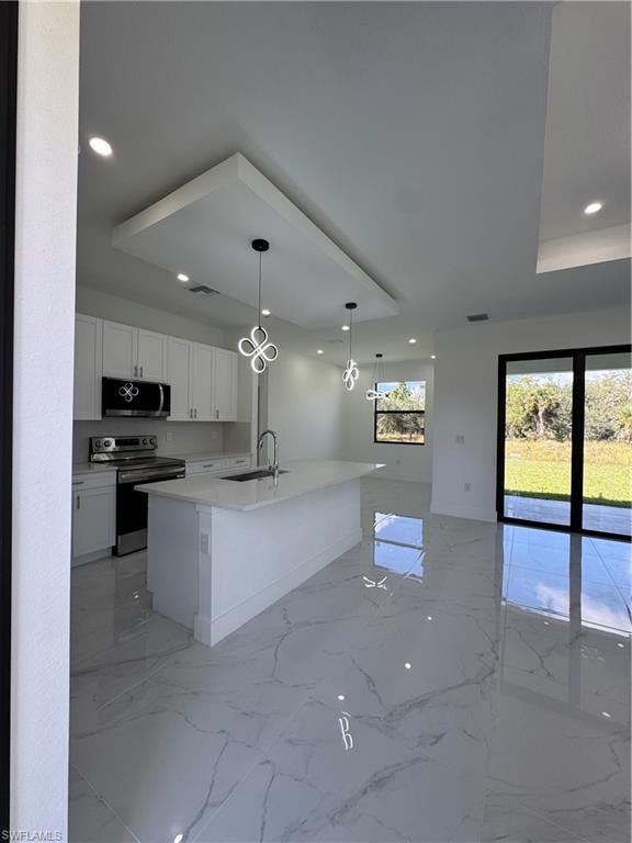 Kitchen with white cabinets, range, pendant lighting, a center island with sink, and light stone counters