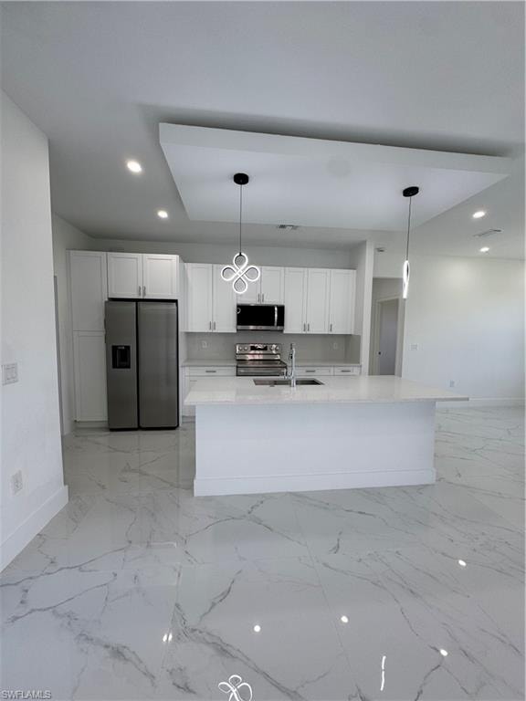 Kitchen with stainless steel appliances, white cabinets, hanging light fixtures, and light stone countertops