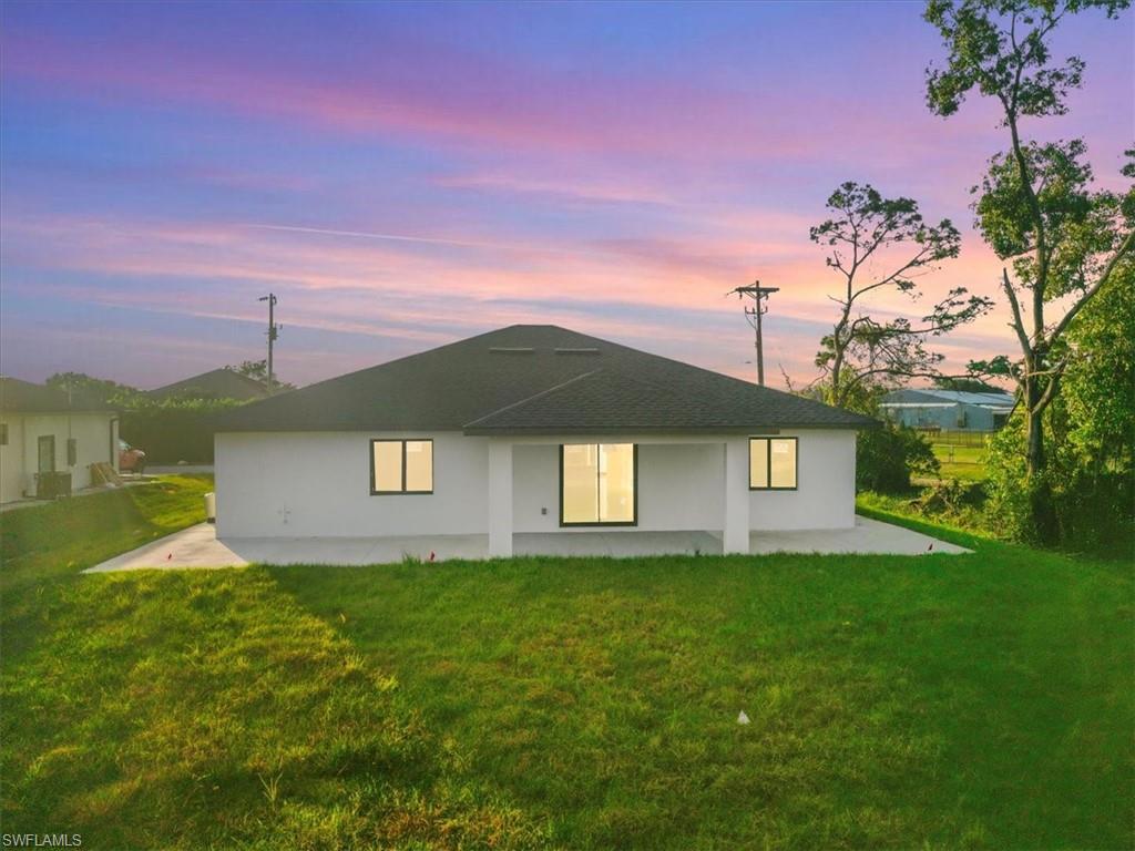 Back of house at dusk featuring a patio area, a yard, and stucco siding