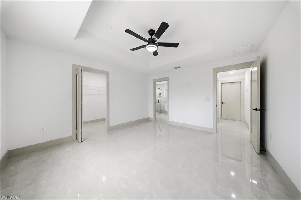 Unfurnished bedroom with a spacious closet, a tray ceiling, ceiling fan, and light tile patterned floors