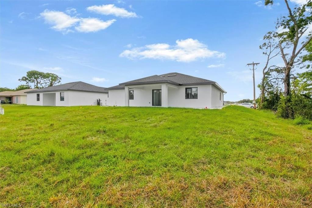 Rear view of house with a lawn, stucco siding, and a patio