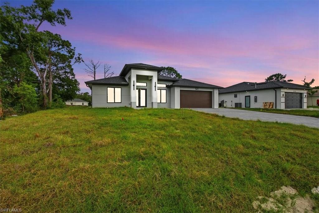 Prairie-style house featuring an attached garage, driveway, a front lawn, and stucco siding
