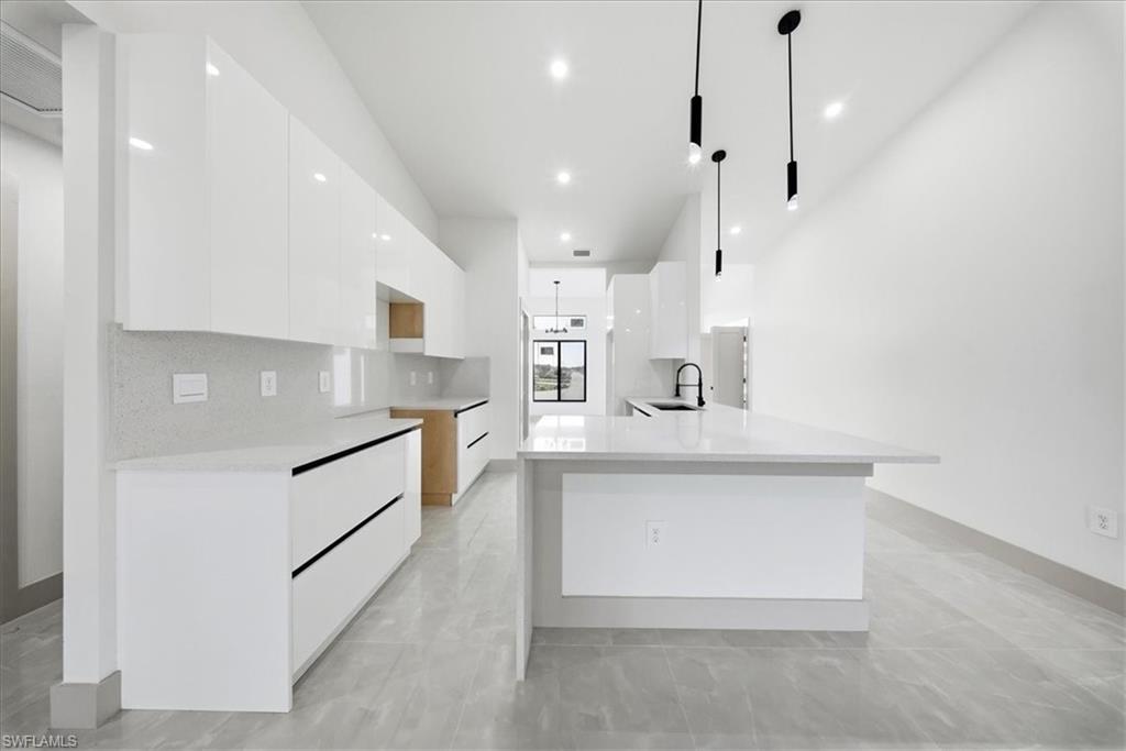 Kitchen with modern cabinets, light stone countertops, white cabinets, and pendant lighting