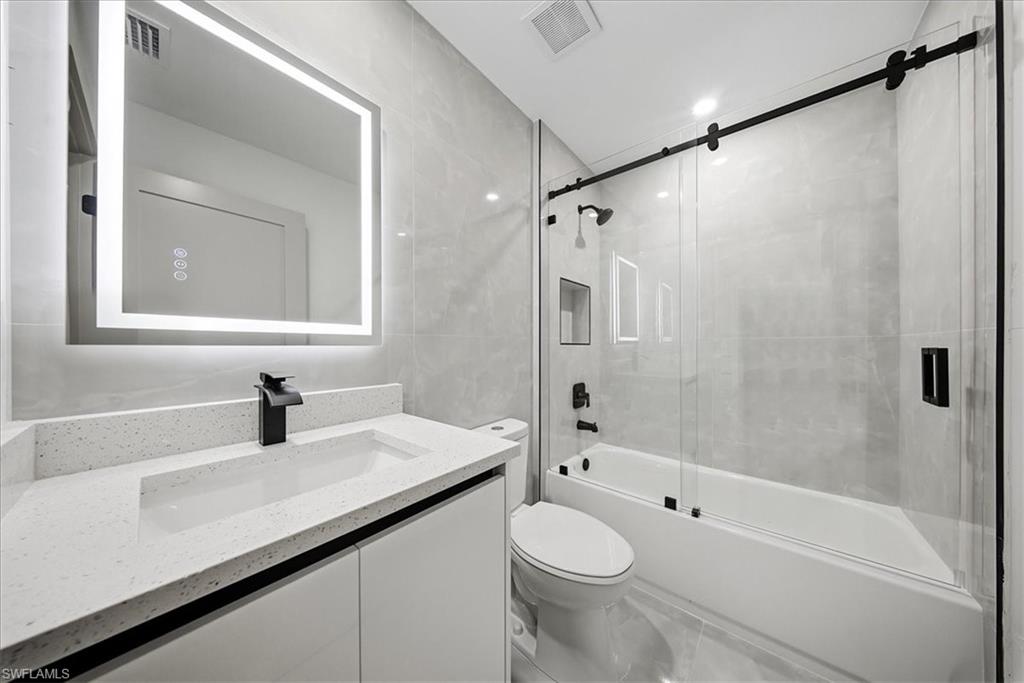Full bath with vanity, tile walls, and enclosed tub / shower combo