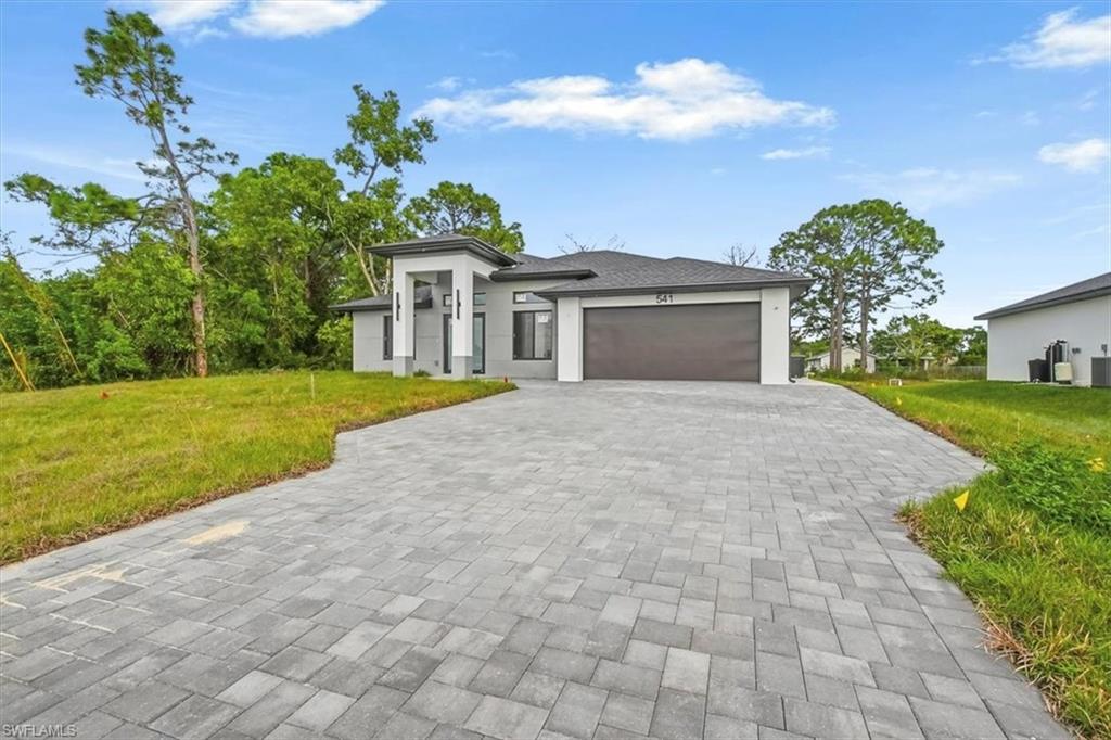 Prairie-style house featuring a front yard, an attached garage, decorative driveway, and stucco siding