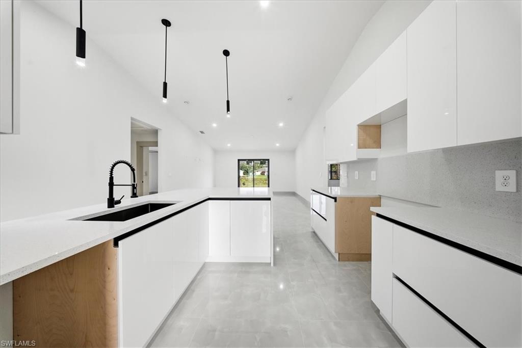 Kitchen featuring white cabinets, modern cabinets, light stone counters, and lofted ceiling