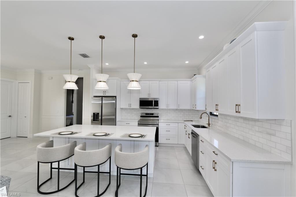 Kitchen featuring stainless steel appliances, crown molding, white cabinetry, a kitchen bar, and a center island