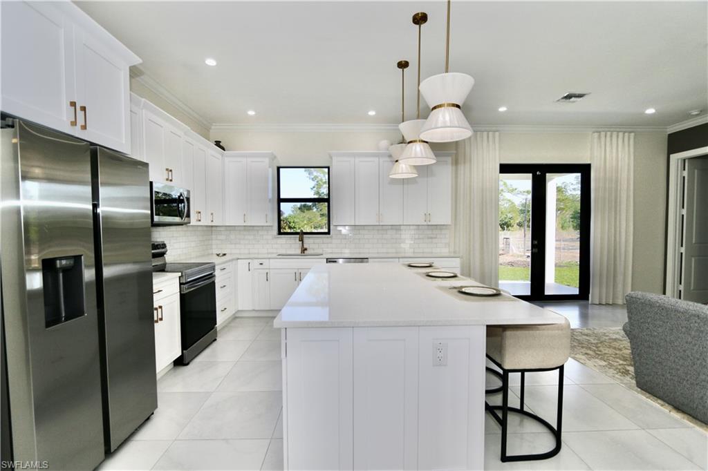 Kitchen with stainless steel appliances, a center island, white cabinets, pendant lighting, and a breakfast bar area