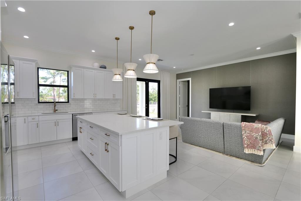Kitchen featuring open floor plan, white cabinets, a center island with sink, pendant lighting, and a kitchen bar